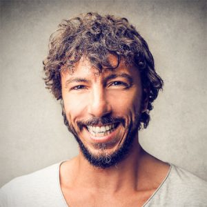 A smiling man with curly hair and a beard, dressed in a light-coloured shirt against a grey background, captures the friendly essence of Kwikshift Removals.